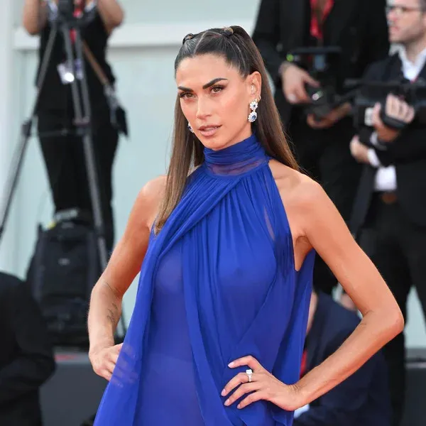 Melissa Satta posa sul red carpet con un abito lungo blu e orecchini pendenti, guardando verso i fotografi.