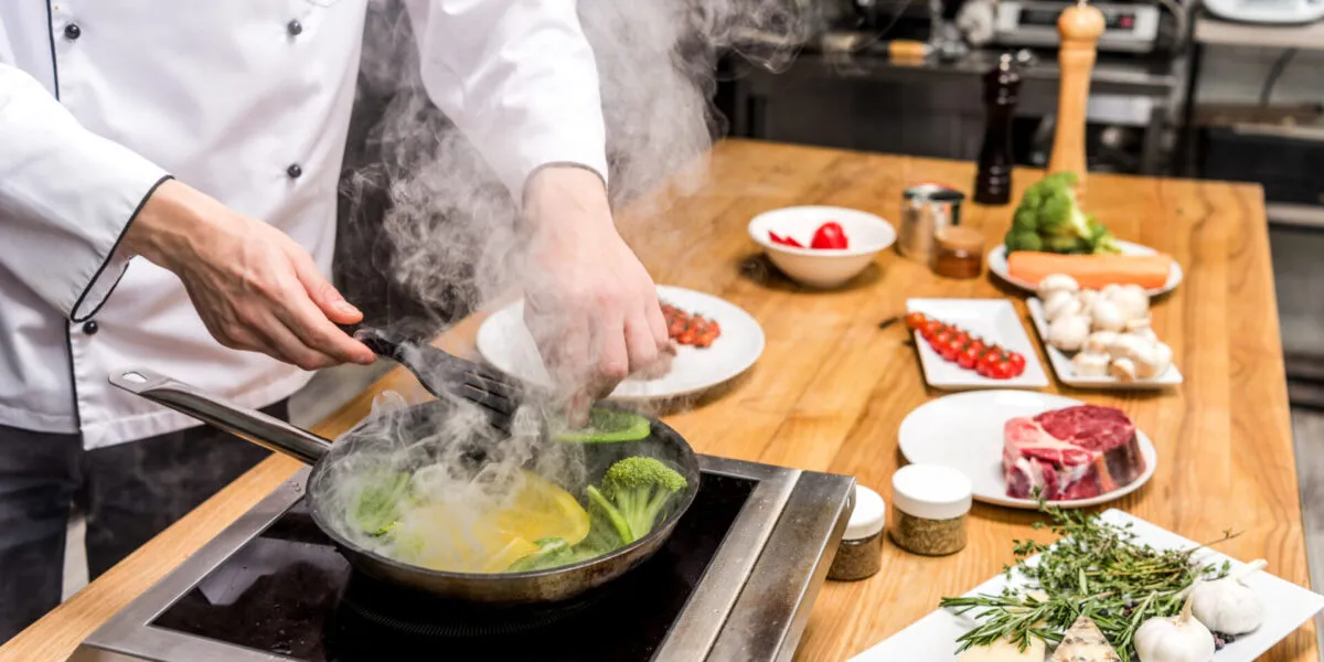 Chef mentre cucina verdure in padella, esempio di metodo di cottura tradizionale utilizzato nella cucina moderna.
