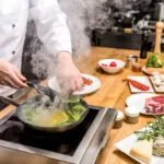Chef mentre cucina verdure in padella, esempio di metodo di cottura tradizionale utilizzato nella cucina moderna.