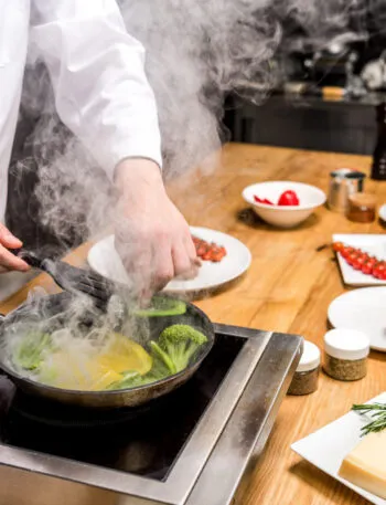 Chef mentre cucina verdure in padella, esempio di metodo di cottura tradizionale utilizzato nella cucina moderna.