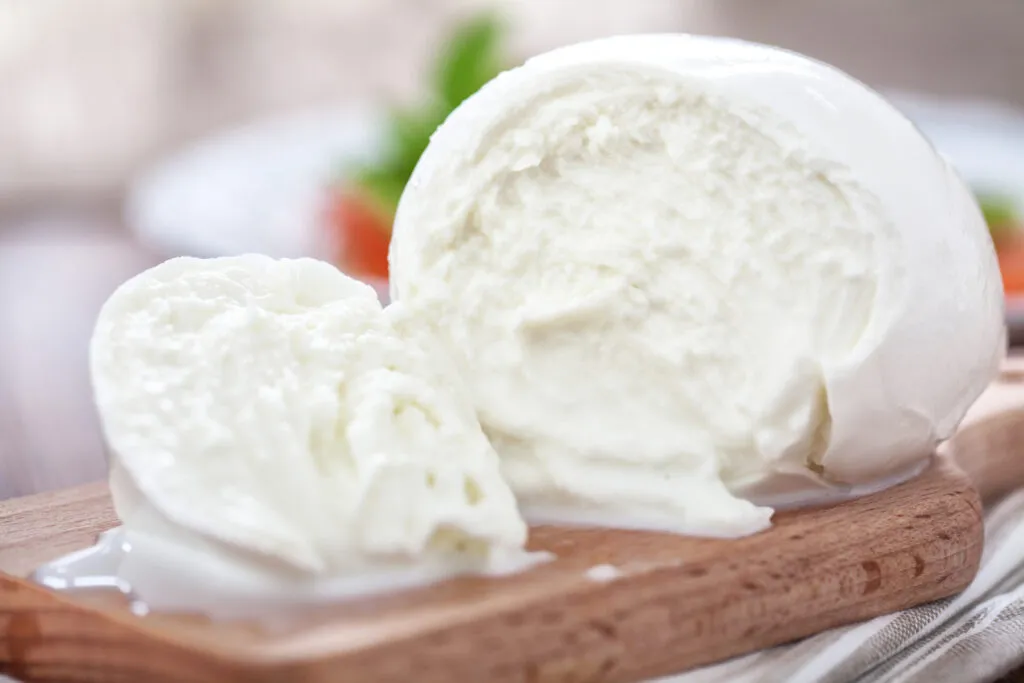 Mozzarella fresca tagliata su tagliere di legno, formaggio ideale per antipasti leggeri e aperitivi estivi.