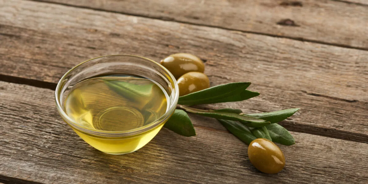 Ciotola di olio extravergine d'oliva con olive e foglie di ulivo su un tavolo in legno, simbolo di un olio EVO di qualità.