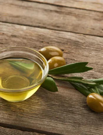 Ciotola di olio extravergine d'oliva con olive e foglie di ulivo su un tavolo in legno, simbolo di un olio EVO di qualità.