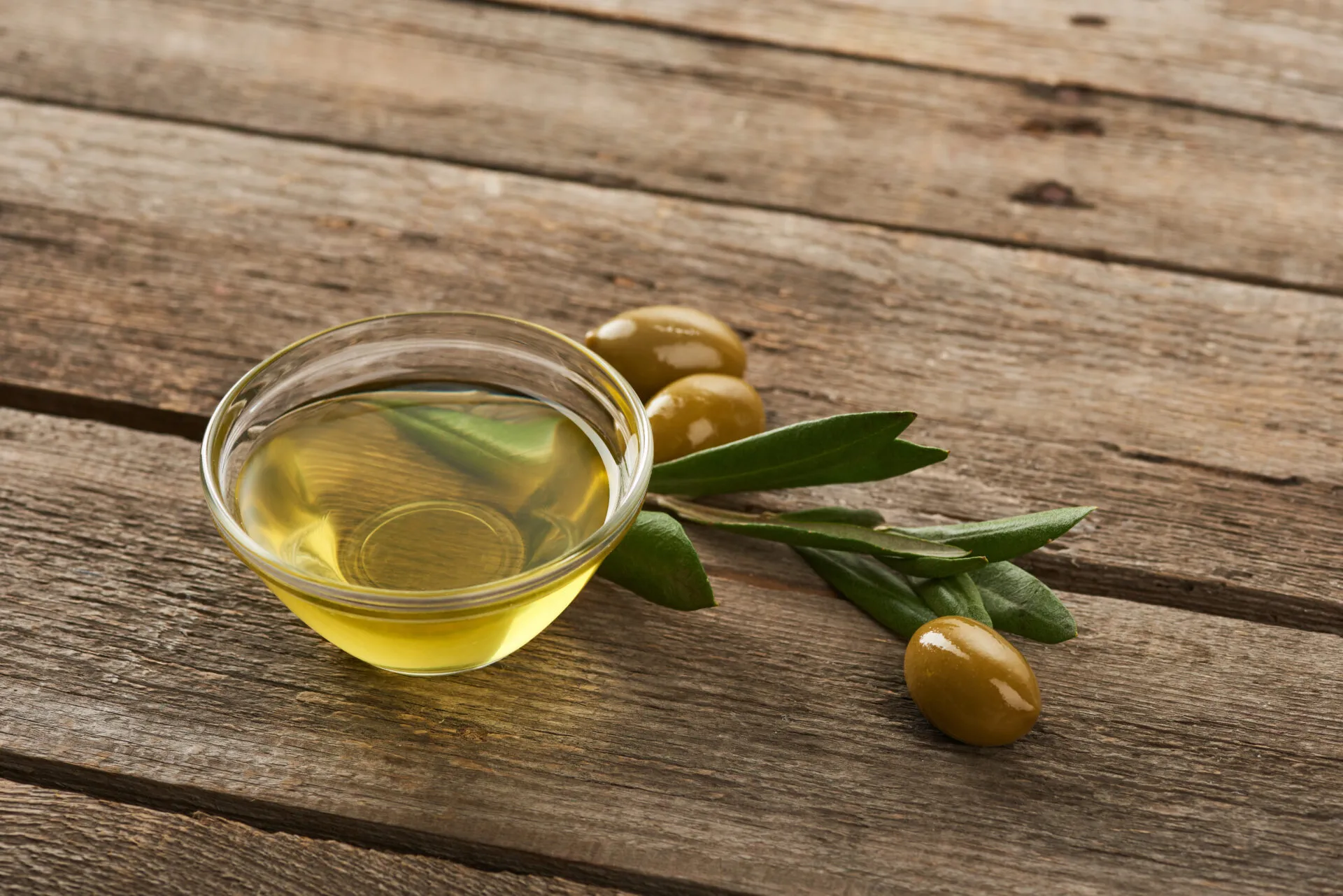 Ciotola di olio extravergine d'oliva con olive e foglie di ulivo su un tavolo in legno, simbolo di un olio EVO di qualità.