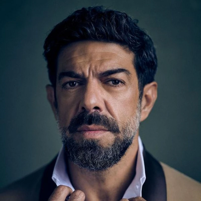 Ritratto di Pierfrancesco Favino con barba e capelli scuri, mentre indossa una giacca elegante e una camicia bianca aperta sul colletto