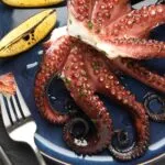 Polpo cotto con limone su piatto blu, confronto tra polpo fresco e polpo surgelato per gusto, tenerezza e qualità.