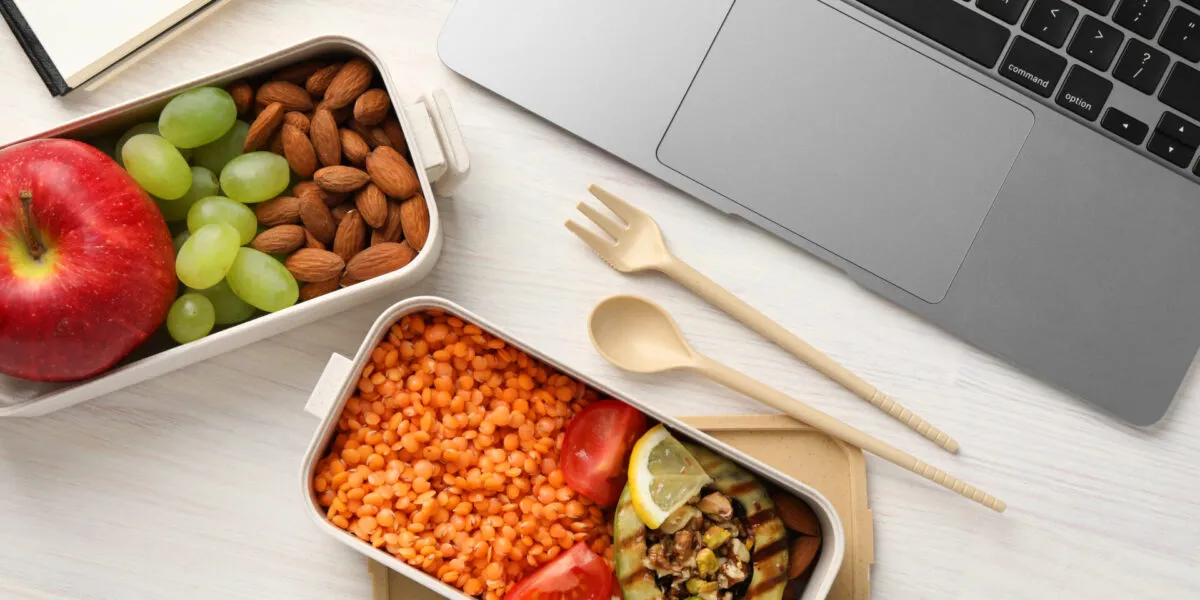 Lunch box per il pranzo in ufficio con lenticchie rosse, melanzana grigliata, pomodorini, mandorle, mela e uva, ideale per un pasto fit e sano.