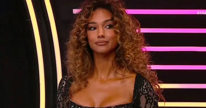 Samira Lui in uno studio televisivo con capelli ricci voluminosi e abito nero in pizzo, mentre guarda lateralmente.