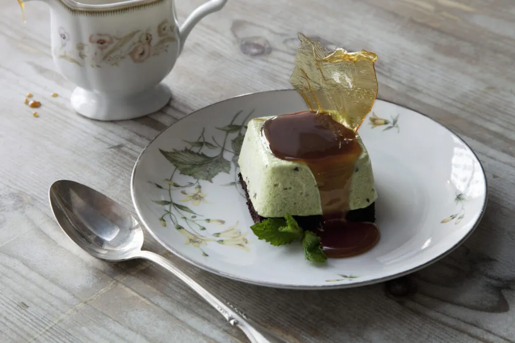 Semifreddo al pistacchio servito su un piatto decorato, accompagnato da salsa al caramello, foglie di menta e decorazione di zucchero croccante.