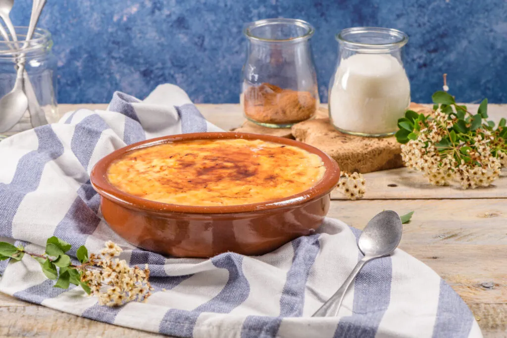Crema catalana servita in una terrina di terracotta con crosta di zucchero caramellato, appoggiata su un tavolo rustico con ingredienti sullo sfondo.