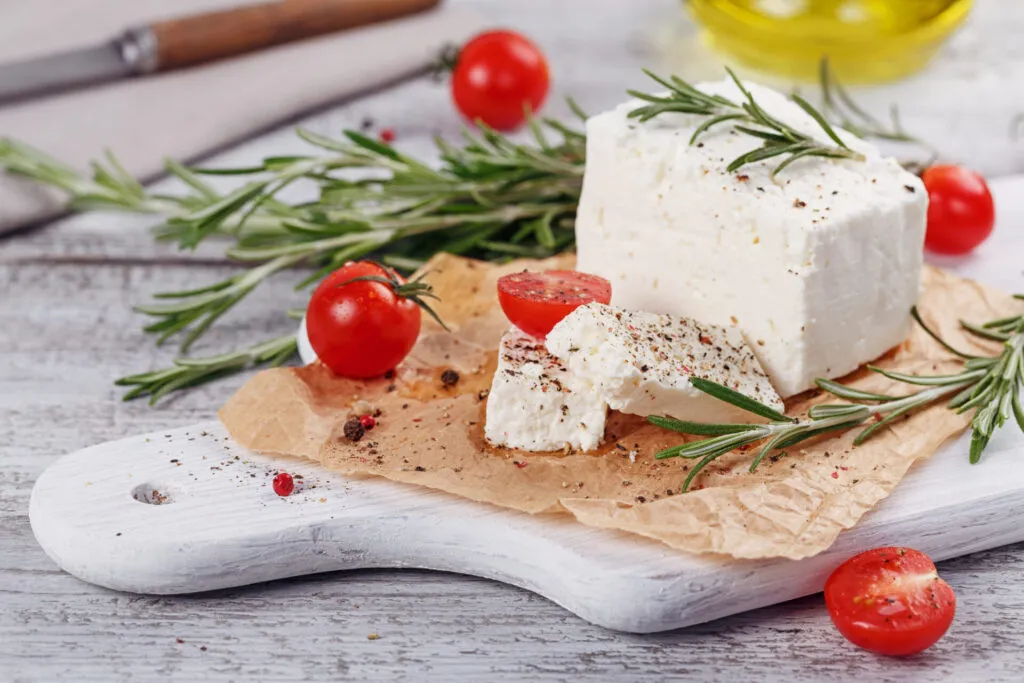 Feta greca con pomodorini e rosmarino su tagliere rustico, formaggio ideale per antipasti e aperitivi mediterranei.