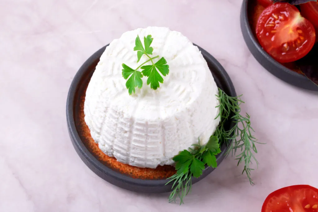 Ricotta fresca con erbe aromatiche e pomodorini, formaggio leggero ideale per antipasti e aperitivi salutari.