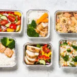 Vaschette con pasti pronti per batch cooking con riso, pollo, salmone, pasta, verdure e insalata.