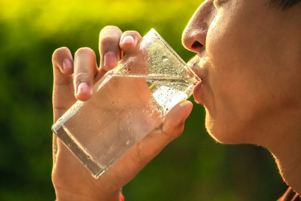 Persona che beve un bicchiere d'acqua per favorire la digestione, l'idratazione e il benessere intestinale.
