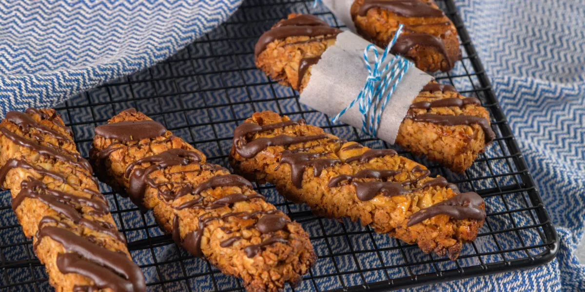 Biscotti fit con avena e frutta secca, decorati con cioccolato e disposti su una griglia.