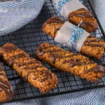 Biscotti fit con avena e frutta secca, decorati con cioccolato e disposti su una griglia.