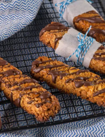 Biscotti fit con avena e frutta secca, decorati con cioccolato e disposti su una griglia.