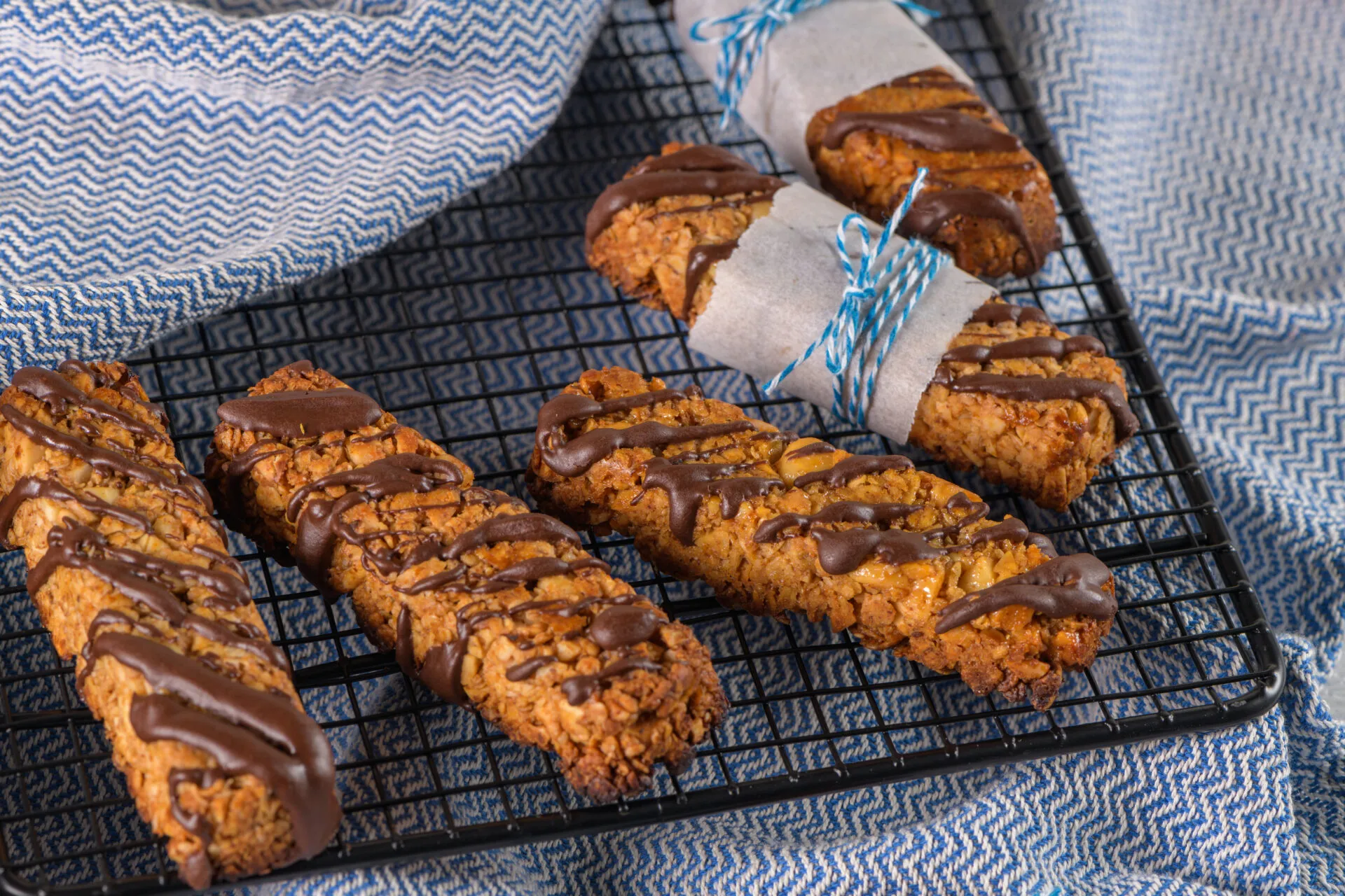 Biscotti fit con avena e frutta secca, decorati con cioccolato e disposti su una griglia.