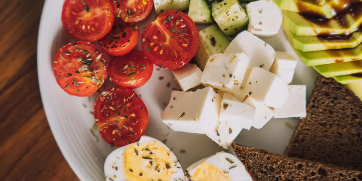 Piatto per colazione salata fit con uova sode, avocado, pomodorini, cetrioli, formaggio a cubetti e pane integrale.