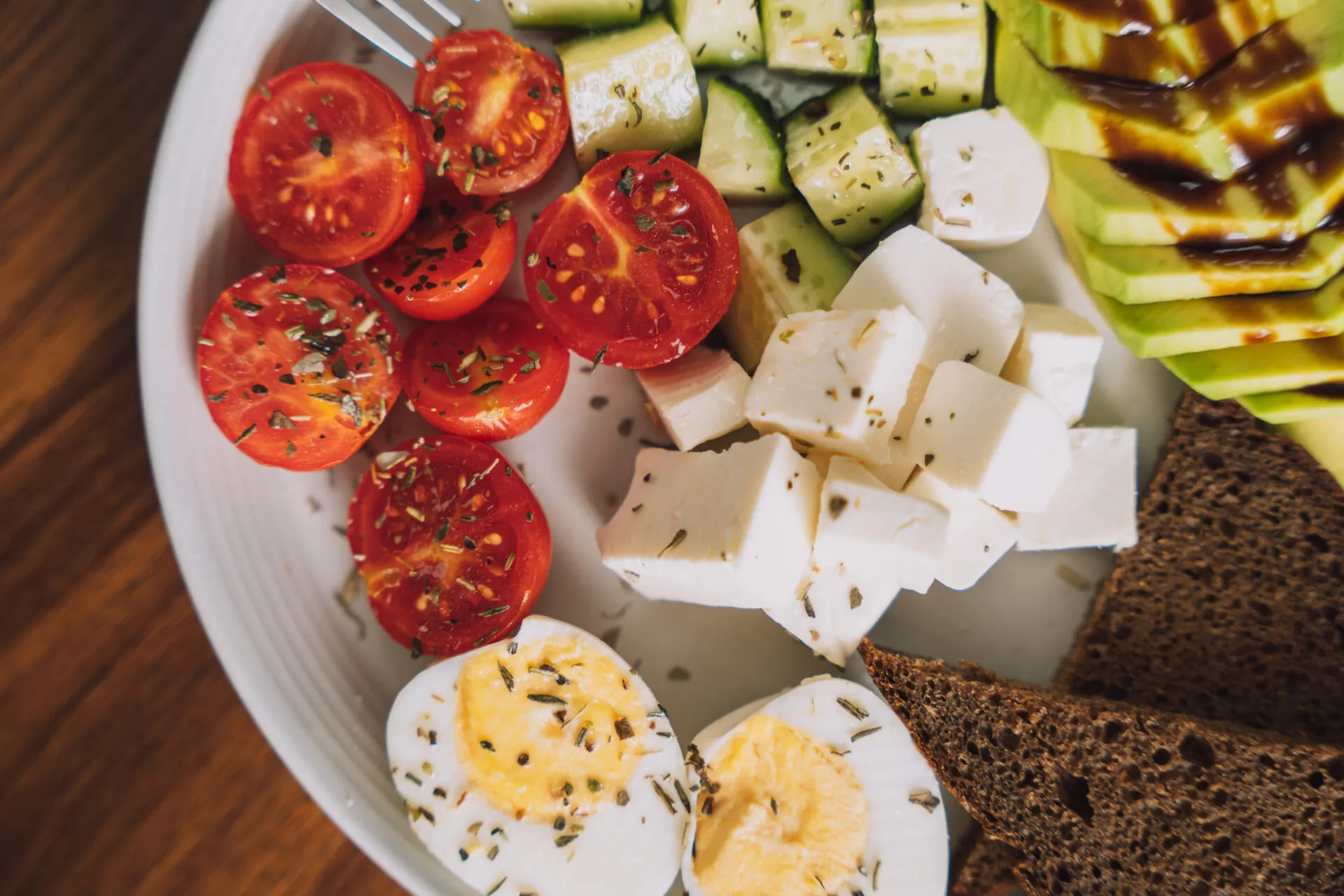 Piatto per colazione salata fit con uova sode, avocado, pomodorini, cetrioli, formaggio a cubetti e pane integrale.