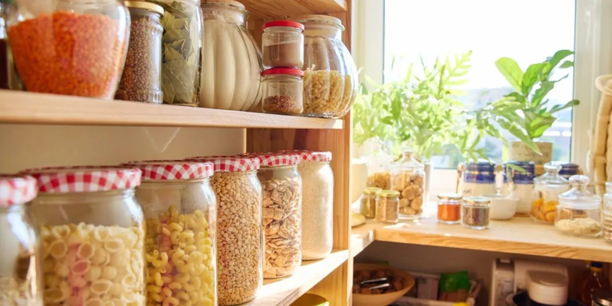 Dispensa fit organizzata con barattoli di vetro pieni di cereali, pasta, legumi e ingredienti sani per ricette equilibrate