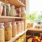 Dispensa fit organizzata con barattoli di vetro pieni di cereali, pasta, legumi e ingredienti sani per ricette equilibrate