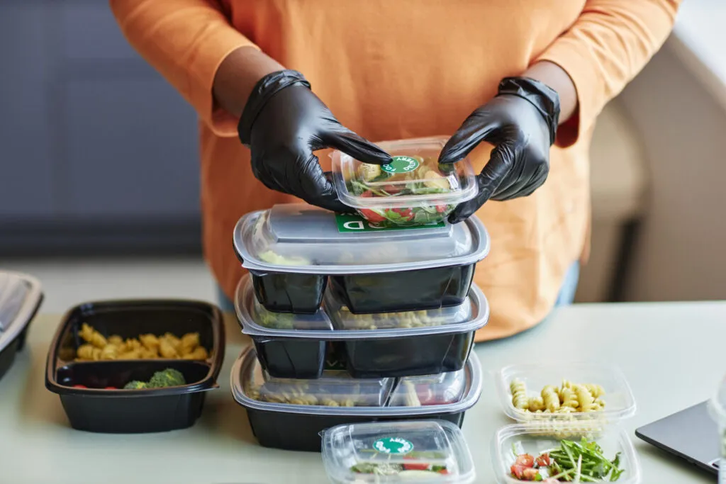 Persona con guanti che impila contenitori con pasti pronti per batch cooking e meal prep.