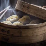 Cottura al vapore con cestello in bambù e ravioli avvolti dal vapore caldo