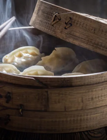 Cottura al vapore con cestello in bambù e ravioli avvolti dal vapore caldo