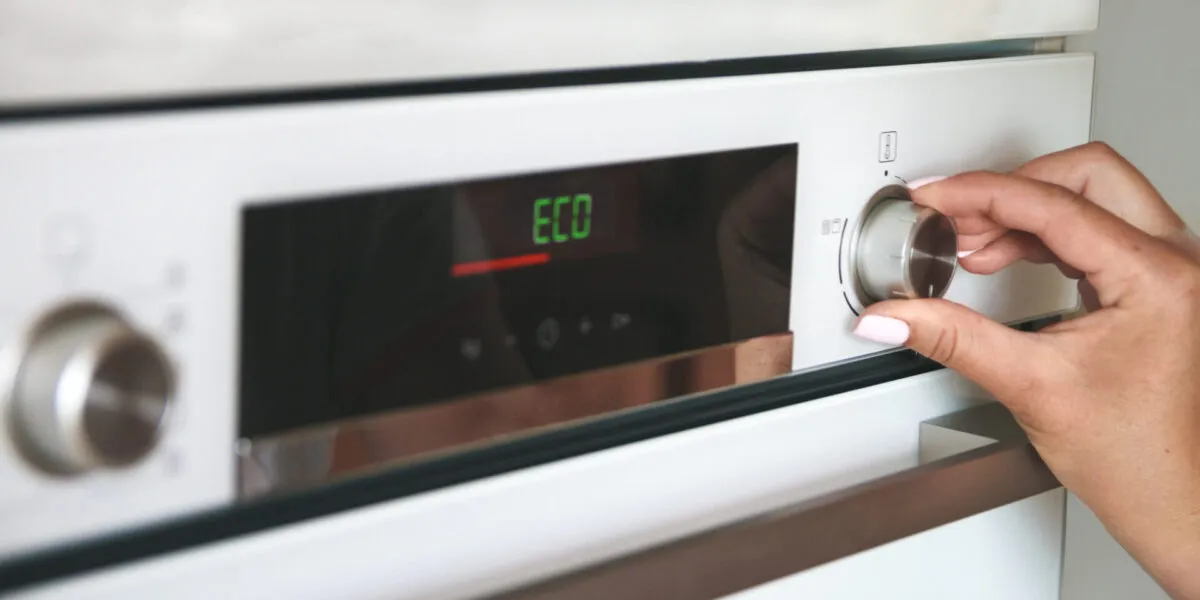 Mano che seleziona la modalità Eco su un forno elettrico per ridurre i consumi energetici in cucina.
