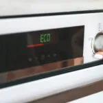 Mano che seleziona la modalità Eco su un forno elettrico per ridurre i consumi energetici in cucina.
