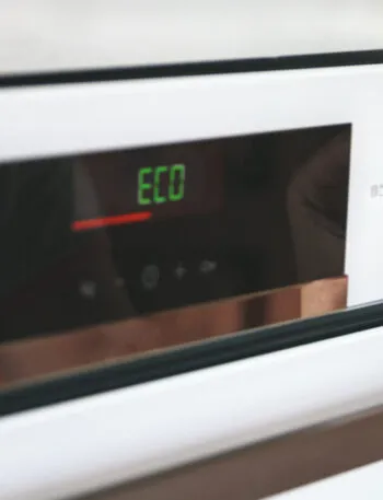 Mano che seleziona la modalità Eco su un forno elettrico per ridurre i consumi energetici in cucina.