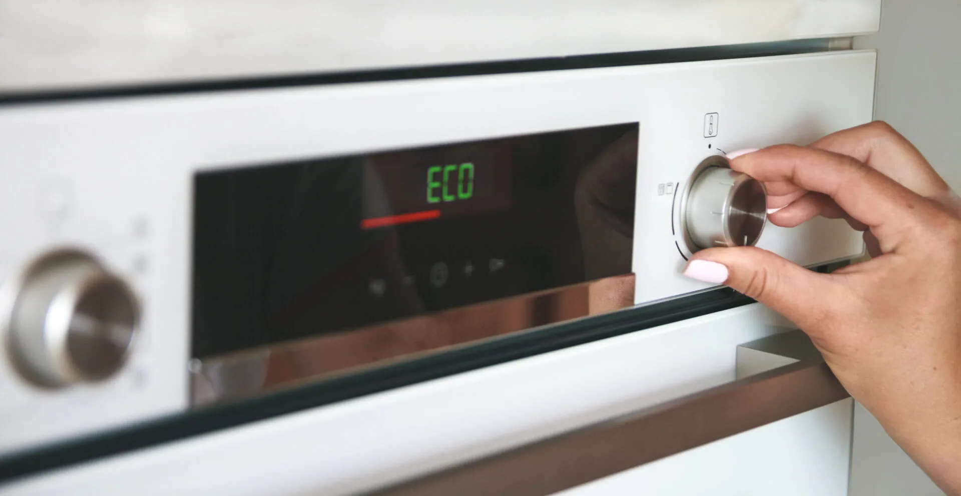 Mano che seleziona la modalità Eco su un forno elettrico per ridurre i consumi energetici in cucina.