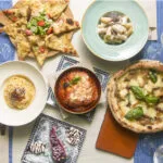 Tavola con piatti della cucina regionale italiana, tra pizza, pasta, parmigiana, focaccia e dolci.