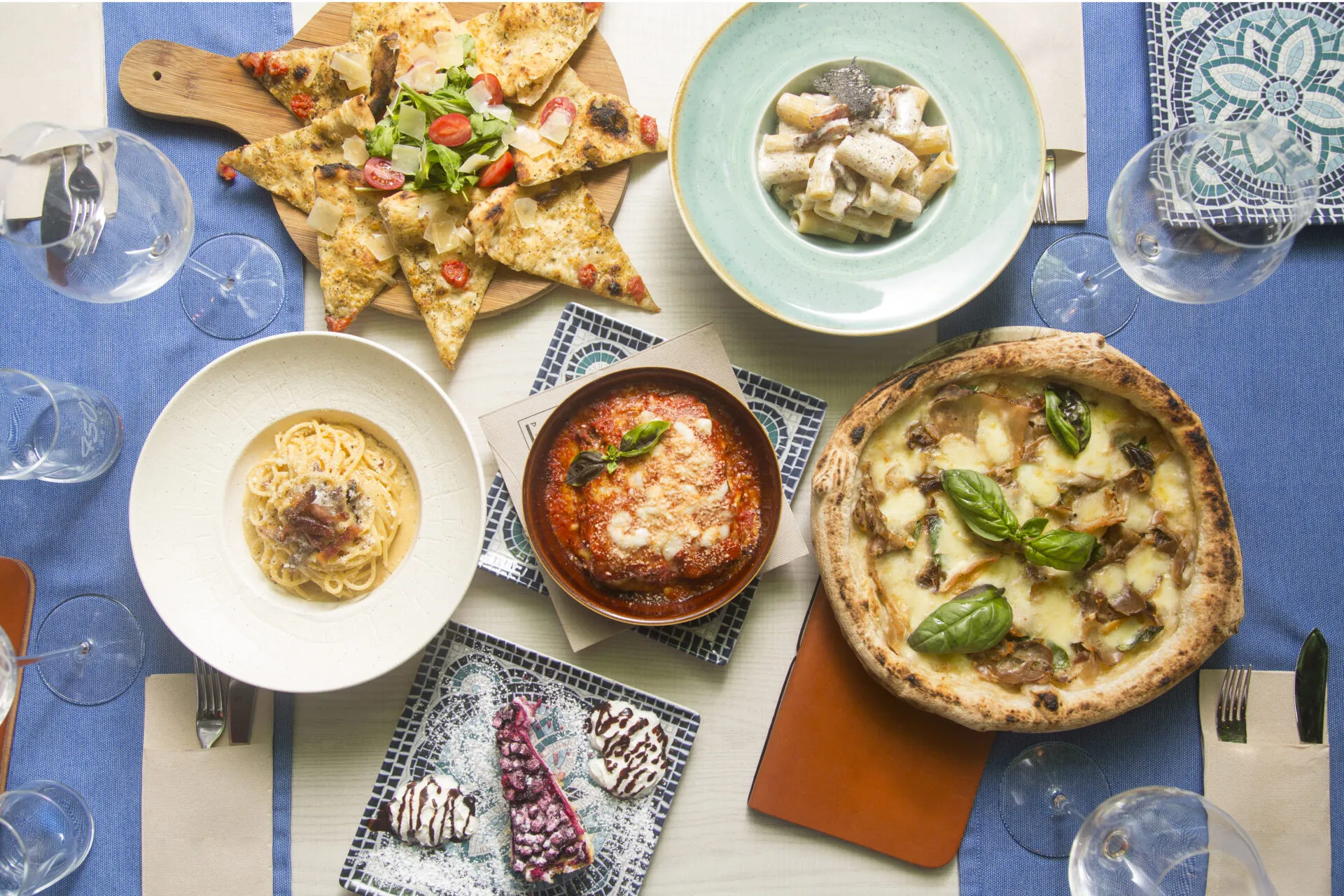 Tavola con piatti della cucina regionale italiana, tra pizza, pasta, parmigiana, focaccia e dolci.