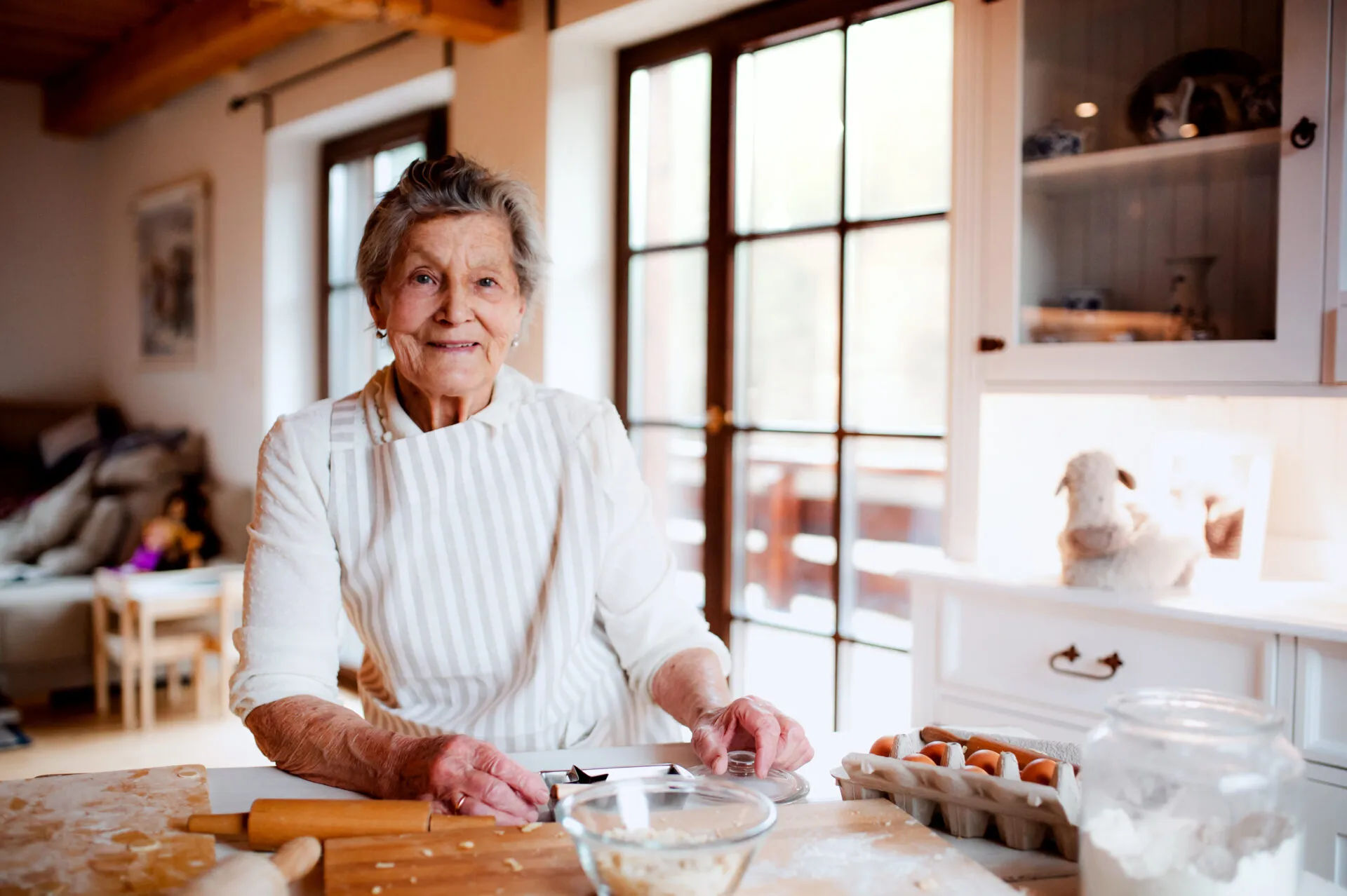 Anziana donna con grembiule prepara un impasto in cucina usando farina, uova e utensili, simbolo del cucinare senza bilancia.