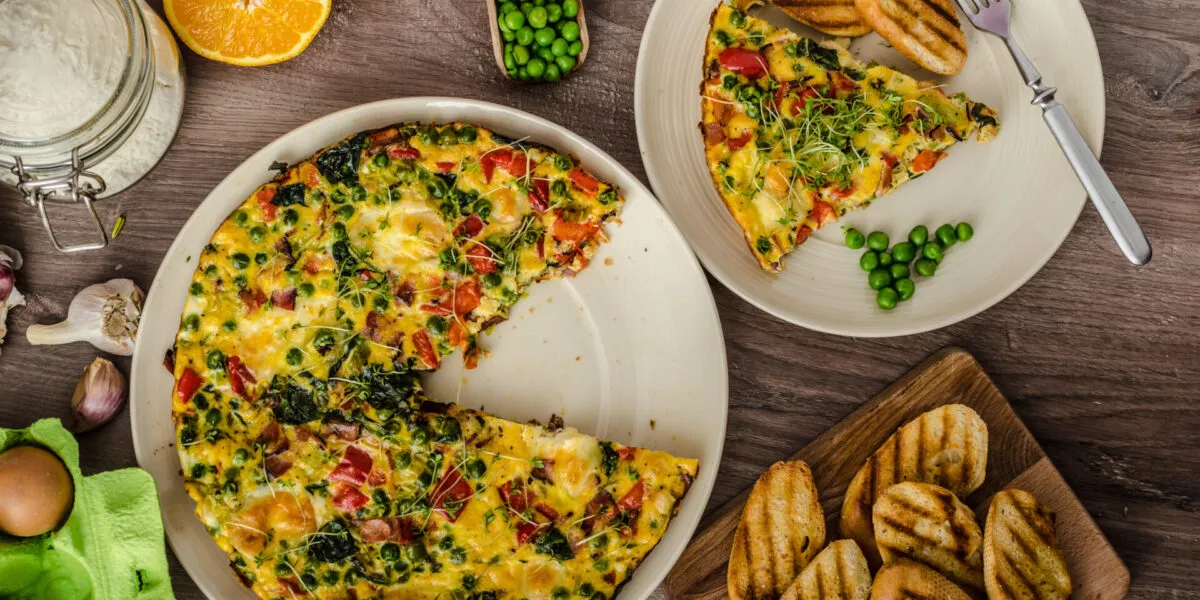 Frittata fit con spinaci, piselli e peperoni, servita a fette con pane tostato su una tavola rustica.