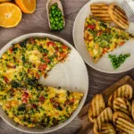 Frittata fit con spinaci, piselli e peperoni, servita a fette con pane tostato su una tavola rustica.