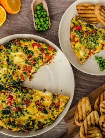 Frittata fit con spinaci, piselli e peperoni, servita a fette con pane tostato su una tavola rustica.