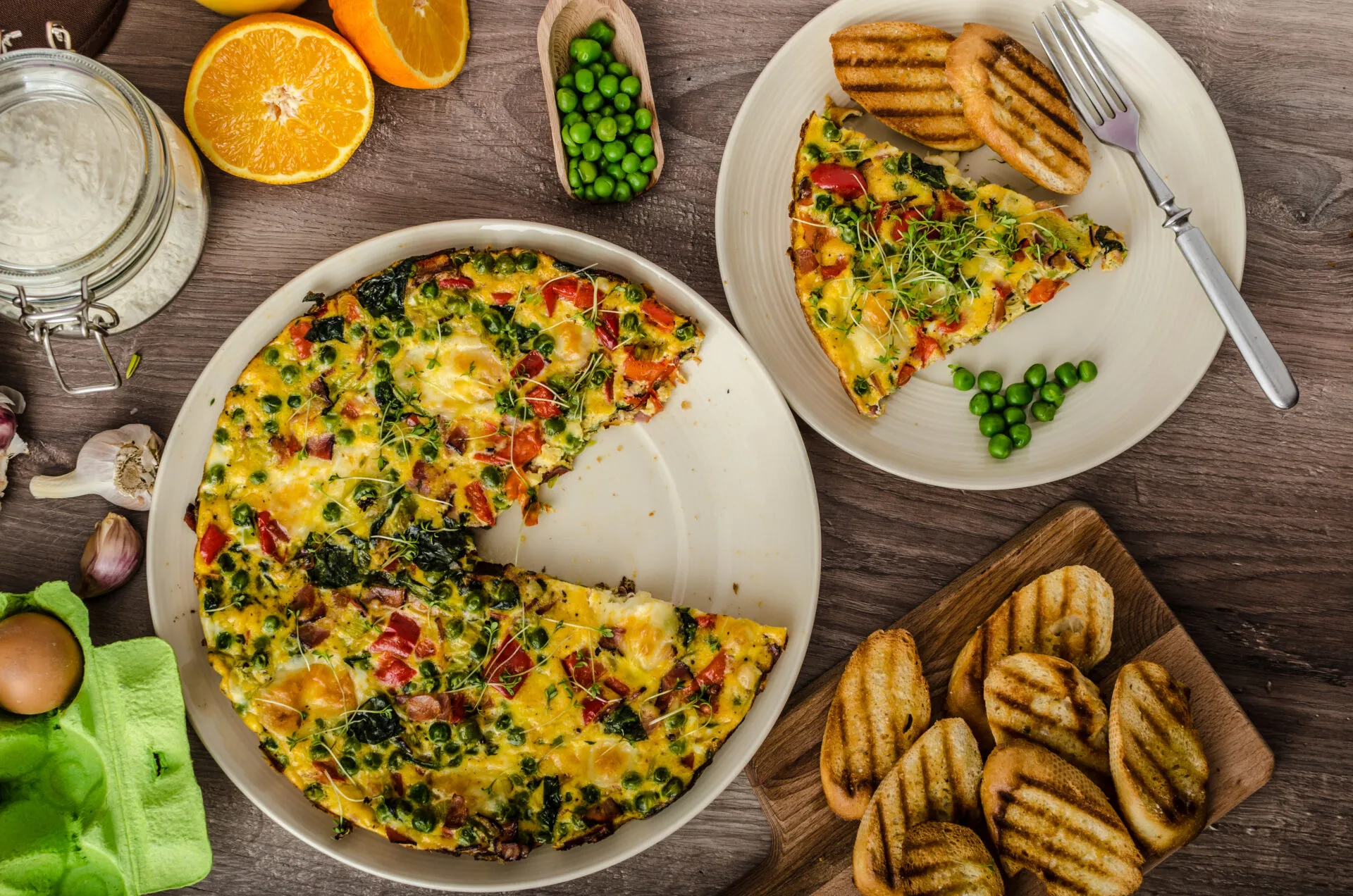 Frittata fit con spinaci, piselli e peperoni, servita a fette con pane tostato su una tavola rustica.
