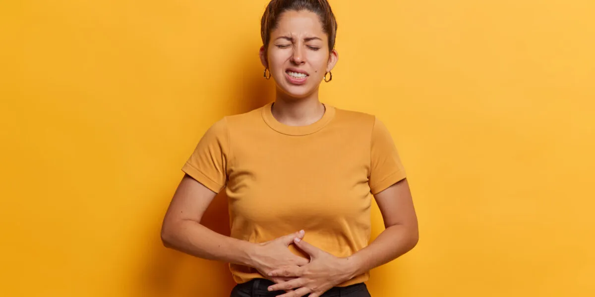 Donna con le mani sull'addome che manifesta dolore e gonfiore addominale, sintomo di digestione lenta e disturbi intestinali.