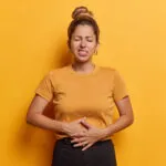 Donna con le mani sull'addome che manifesta dolore e gonfiore addominale, sintomo di digestione lenta e disturbi intestinali.