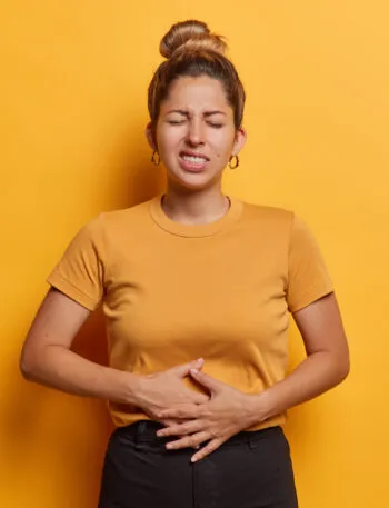 Donna con le mani sull'addome che manifesta dolore e gonfiore addominale, sintomo di digestione lenta e disturbi intestinali.