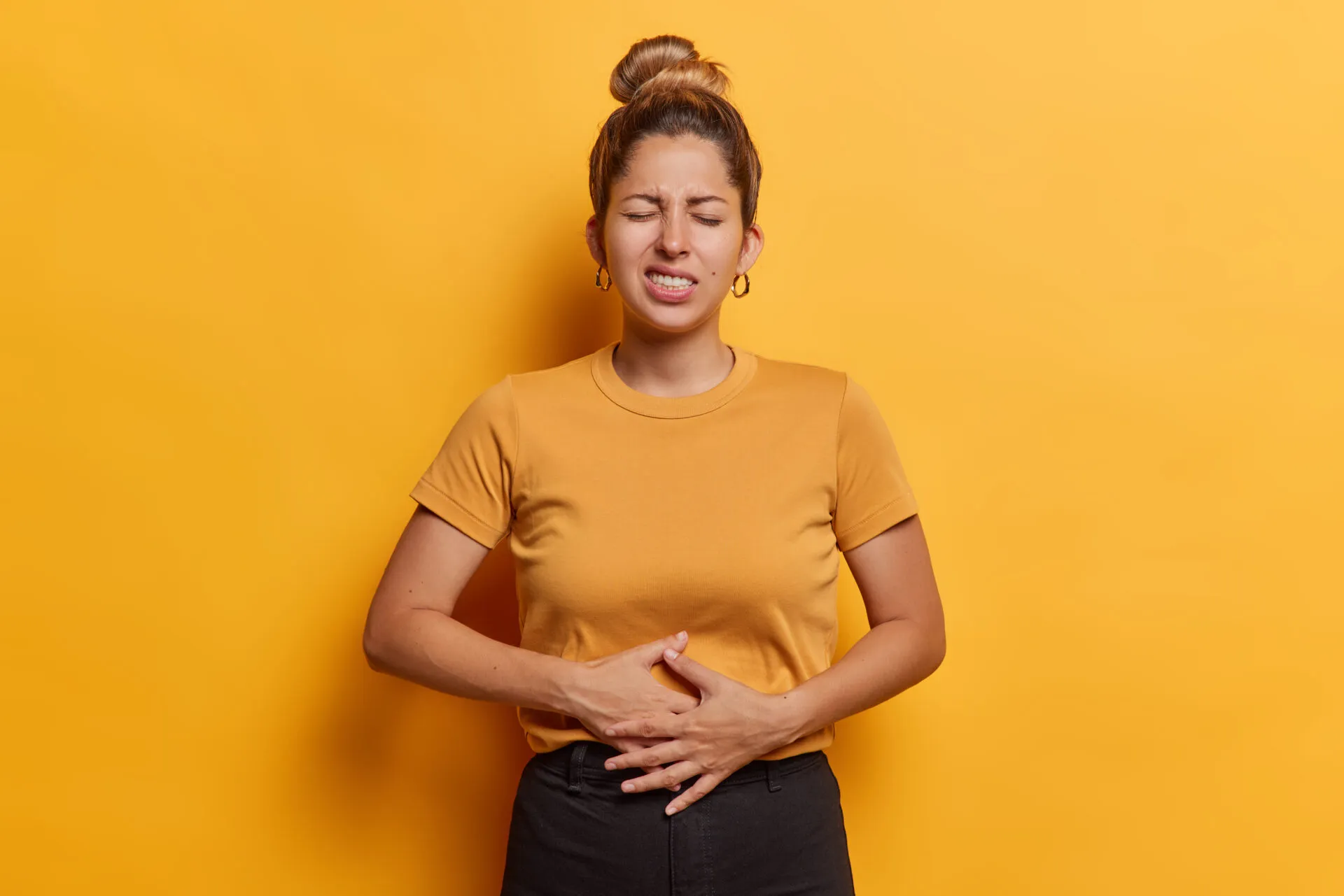 Donna con le mani sull'addome che manifesta dolore e gonfiore addominale, sintomo di digestione lenta e disturbi intestinali.