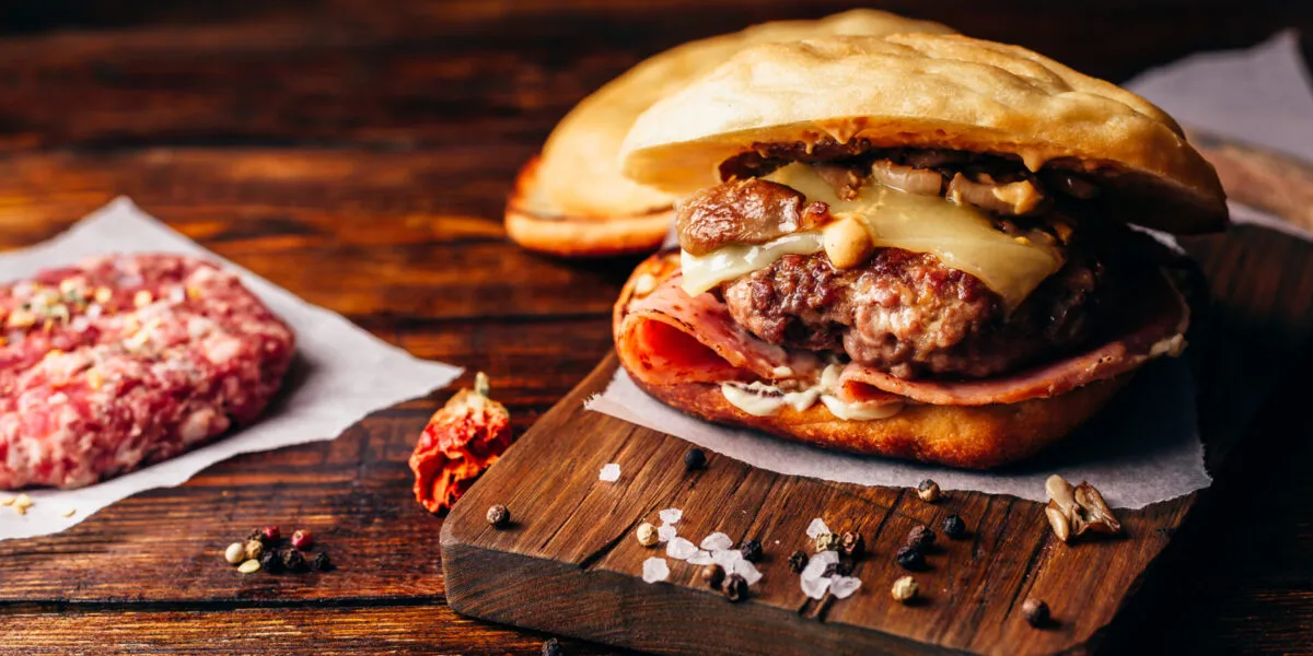 Hamburger fatto in casa con carne, formaggio fuso, funghi e prosciutto su tagliere di legno.