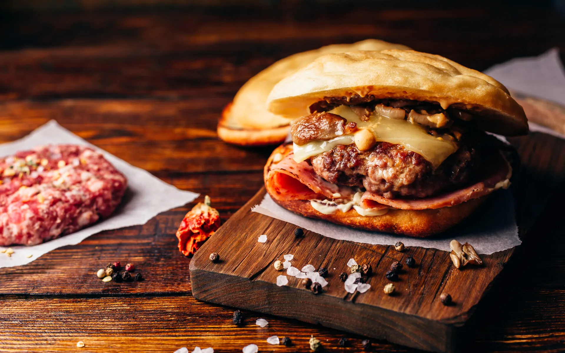 Hamburger fatto in casa con carne, formaggio fuso, funghi e prosciutto su tagliere di legno.