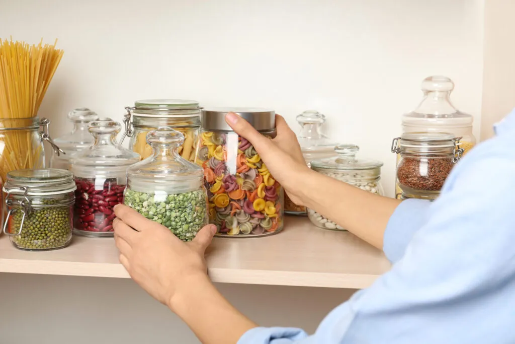 Organizzazione della dispensa fit con barattoli di vetro contenenti pasta, legumi, cereali e ingredienti sani