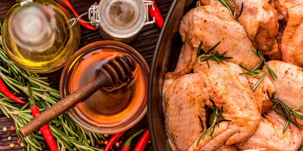 Pollo marinato con rosmarino e spezie, affiancato da miele, olio, peperoncini e pomodori.