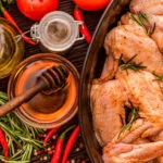 Pollo marinato con rosmarino e spezie, affiancato da miele, olio, peperoncini e pomodori.