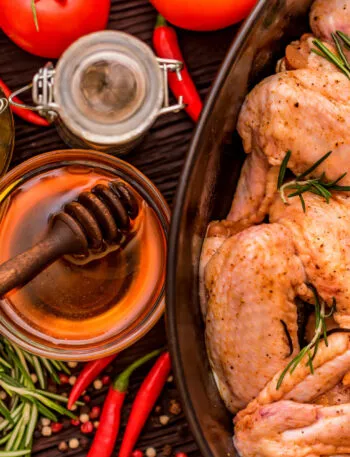 Pollo marinato con rosmarino e spezie, affiancato da miele, olio, peperoncini e pomodori.